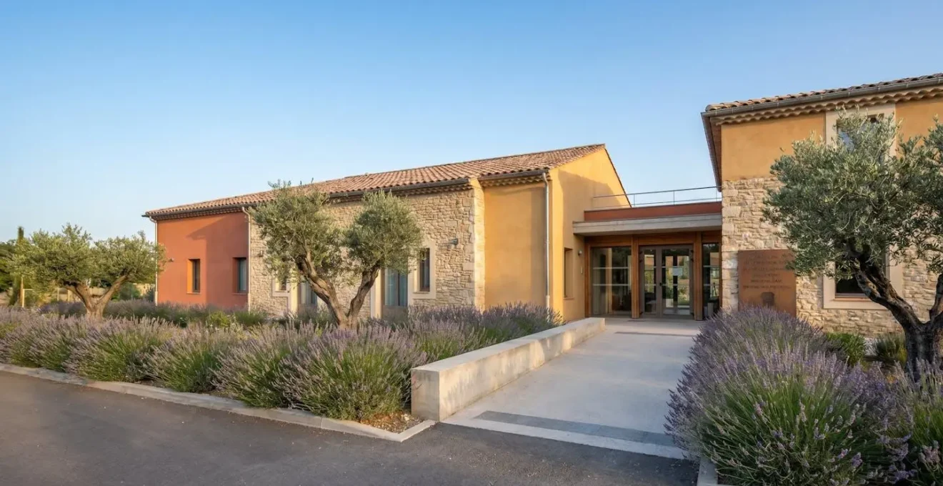 Façade d'un établissement EHPAD de style provençal avec entrée accessible, entouré de végétation méditerranéenne sous ciel bleu